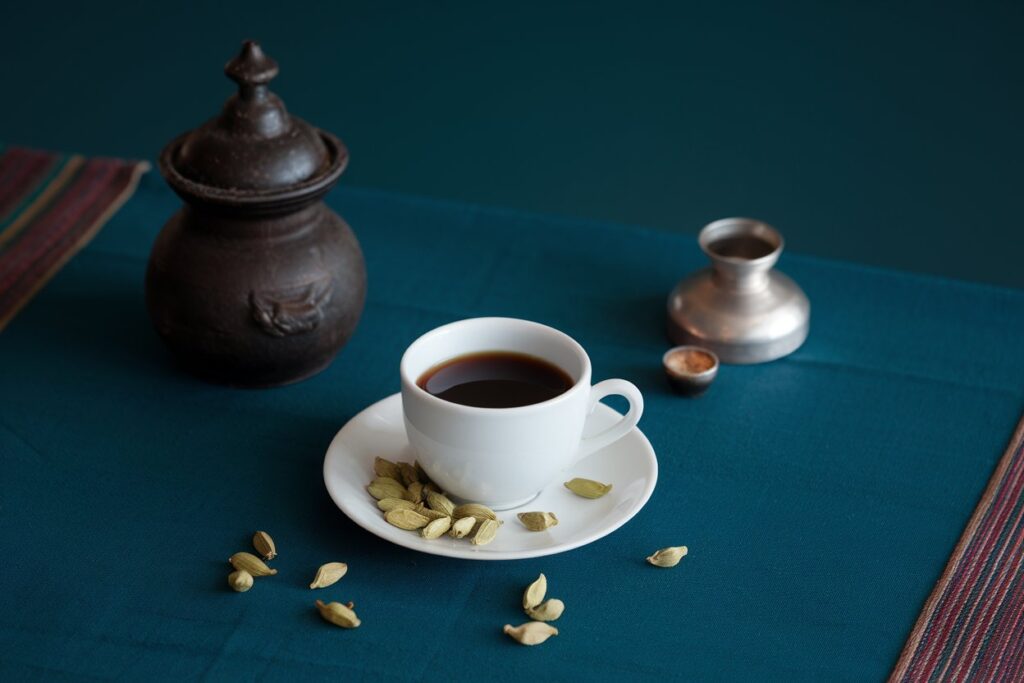 Tasse Kaffee mit Kardamomkapseln auf einem dekorativen Stoff – ein Beispiel, um Kaffee mit Gewürzen zu verfeinern.