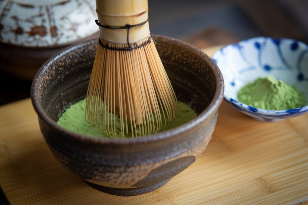 Matcha-Tee in einer traditionellen Teetasse mit einem Matcha-Besen auf einer Bambusunterlage.